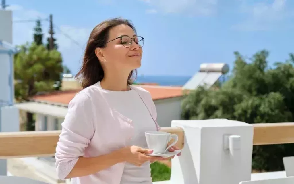 Gyerek nélkül 50 felett: megbánták? Mosolygó középkorú nő kávéscsészével egy napsütötte teraszon